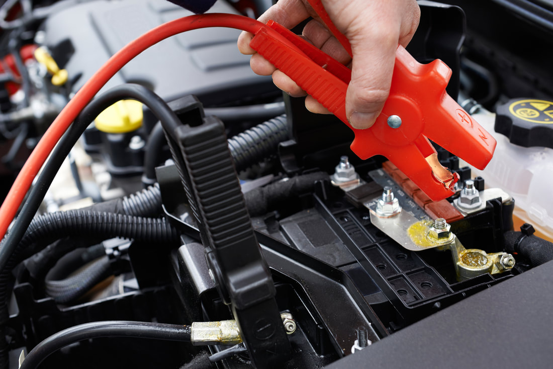 brockton tow truck driver placing jumper cables on car battery to jumpstart car